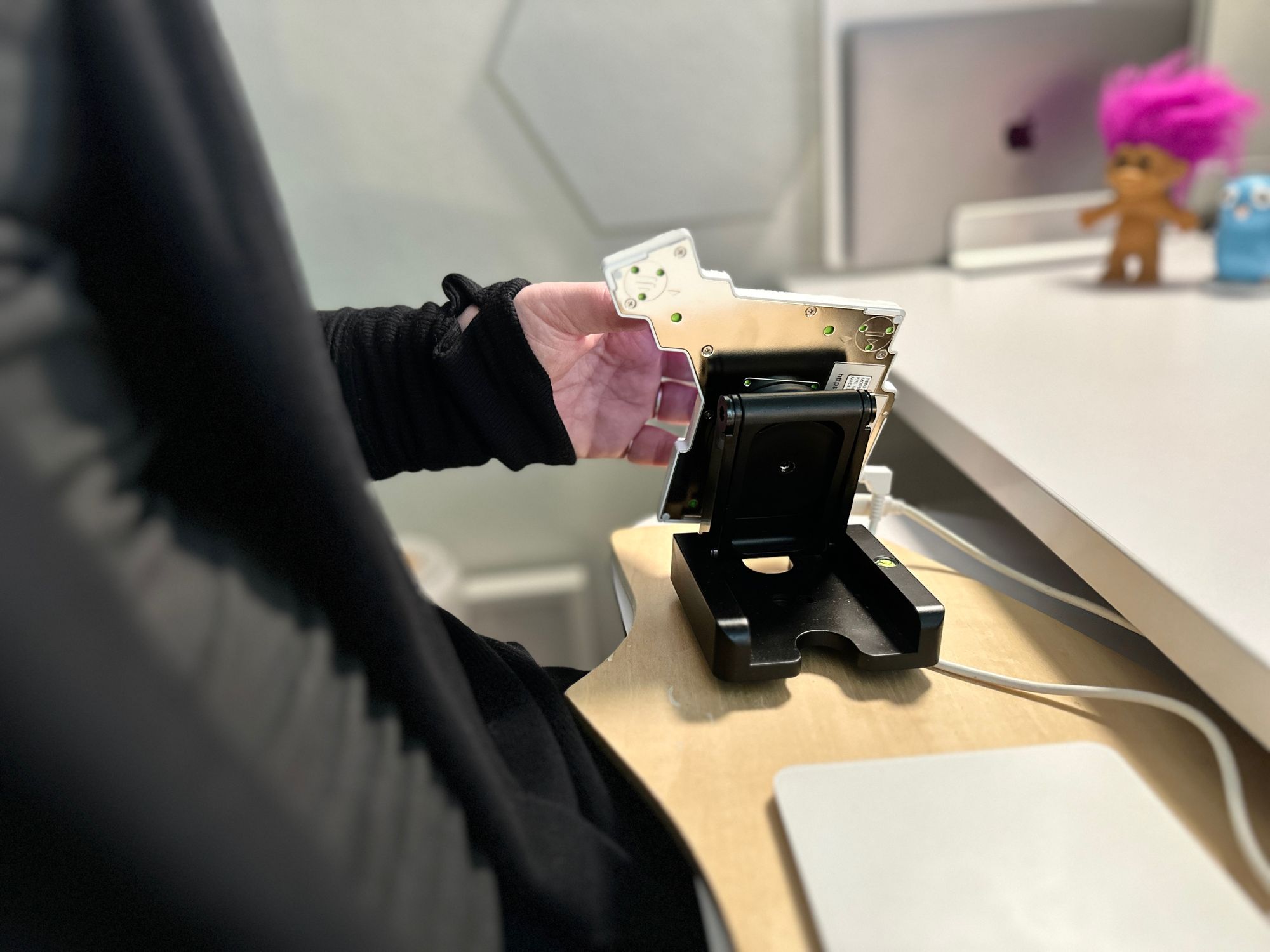 Half of a split keyboard, magnetically attached to a folding stand on a wooden board, which rests on a keyboard tray on a white desk. The stand tents the keyboard very steeply, keeping the wrist of the person using it neutral.