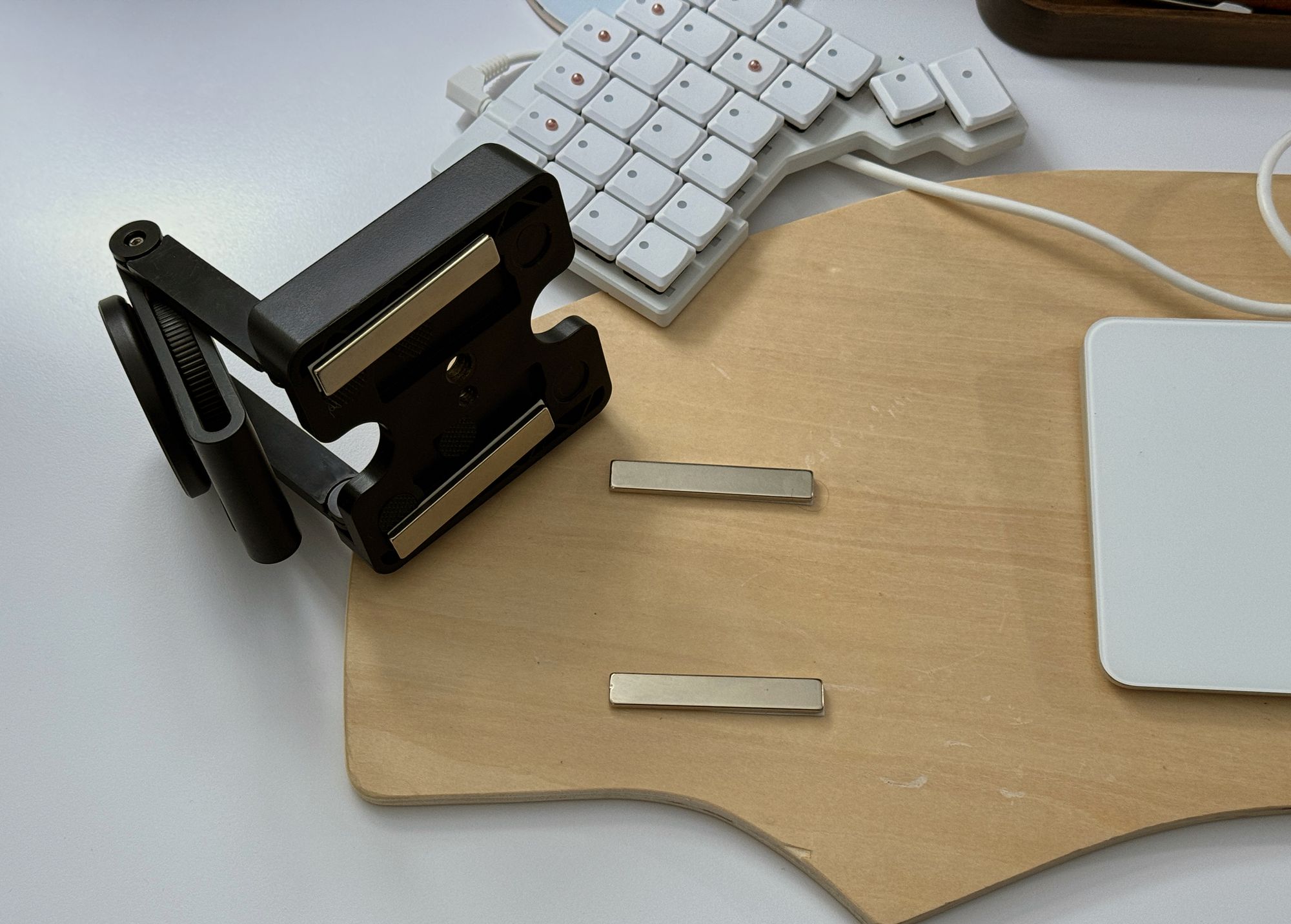 Black Z-shaped camera mount with two silver bar nagnets stuck to its base, next to a lap desk with corresponding bar bar nagnets for the mount to attach to.