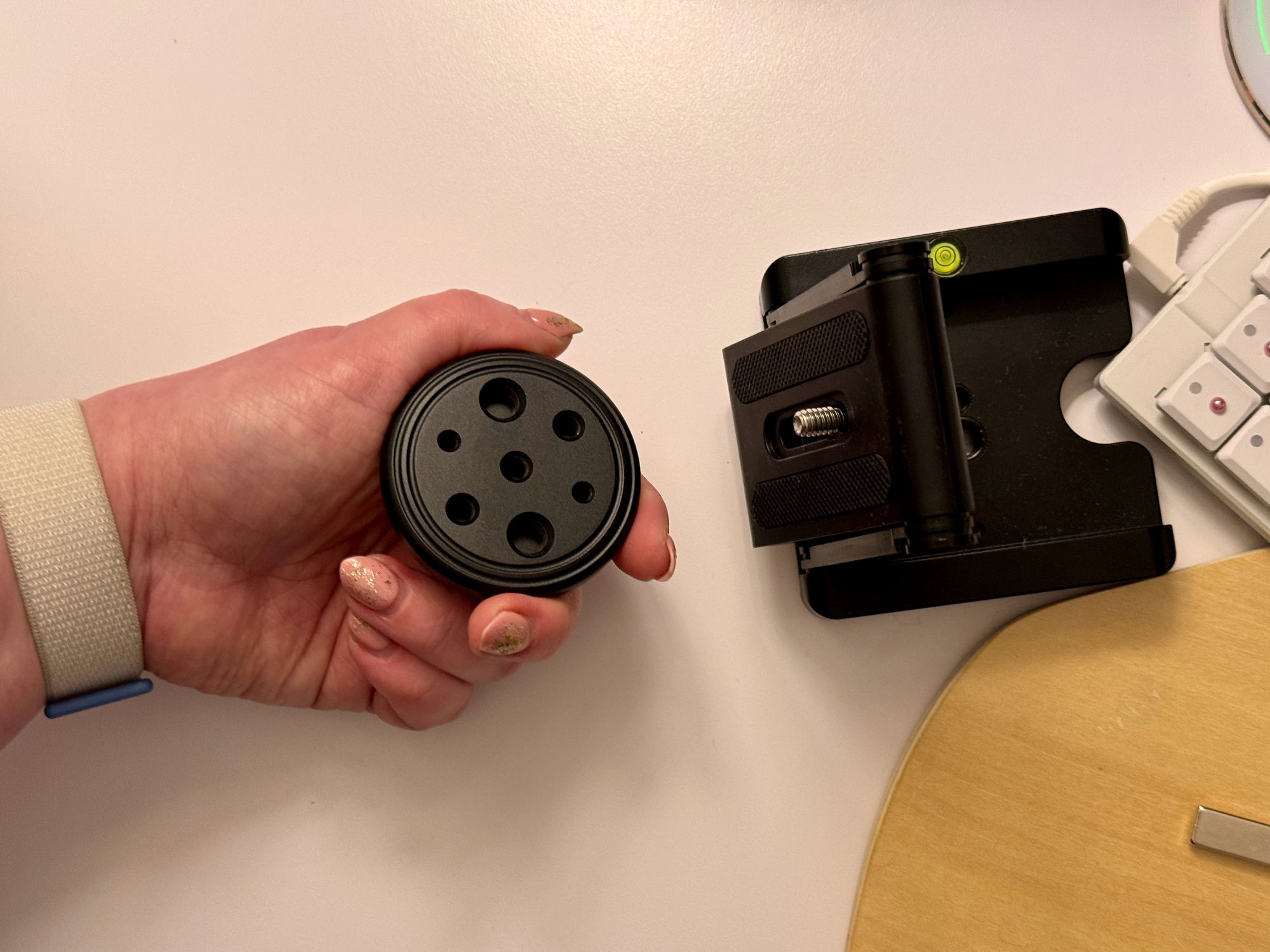 Hand holding a MagSafe tripod mount. The center of the tipod mount has a hole for the screw on the Z-shaped mount to attach to.