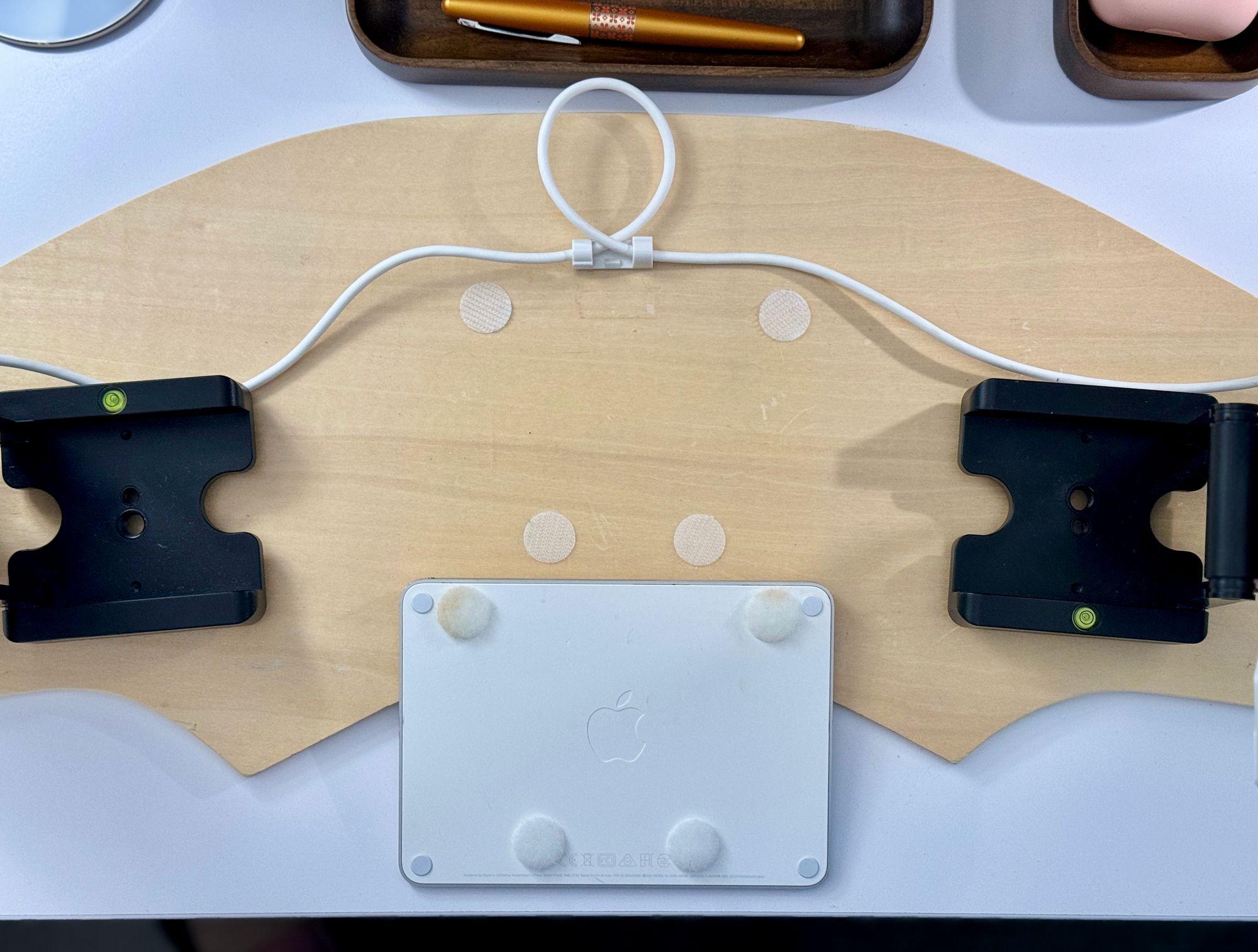 A white trackpad lying with its back side up, which has four Velcro dots stuck to it. It rests on a lap desk with four corresponding Velcro dots for the trackpad to attach to.
