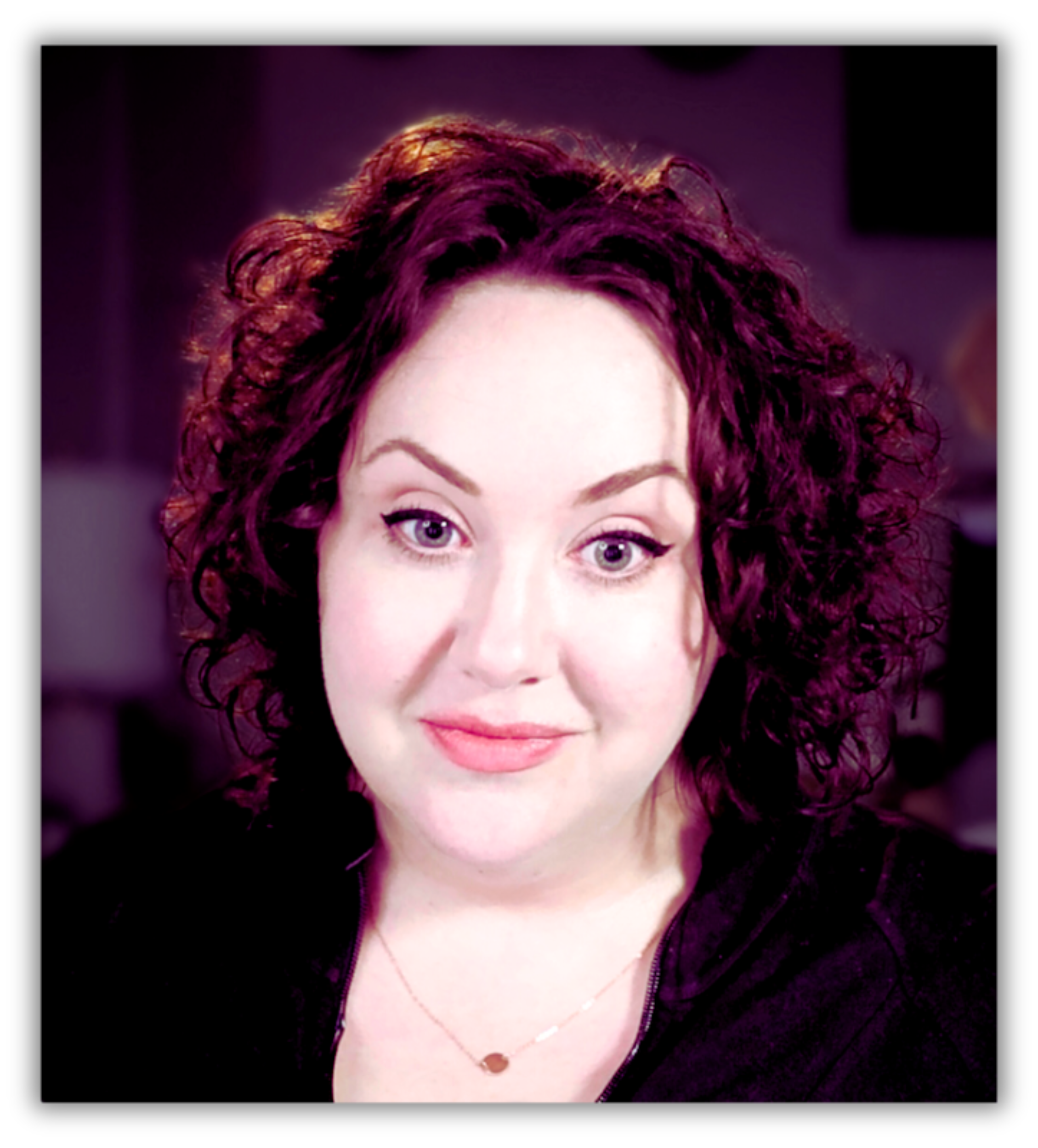White woman with dark curly hair and winged eyeliner, wearing a gold necklace and a black top.